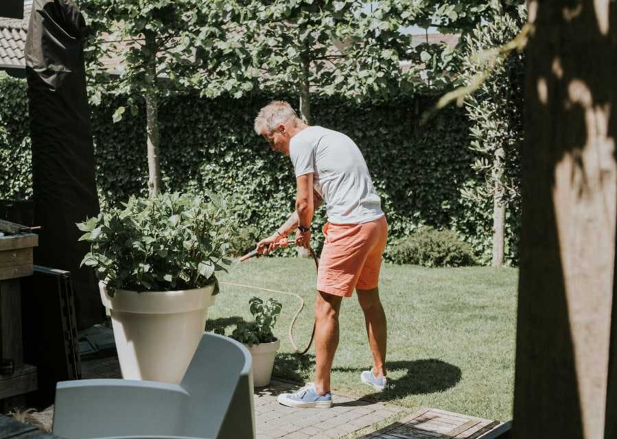 Een man staat in de tuin en bewatert een plant.