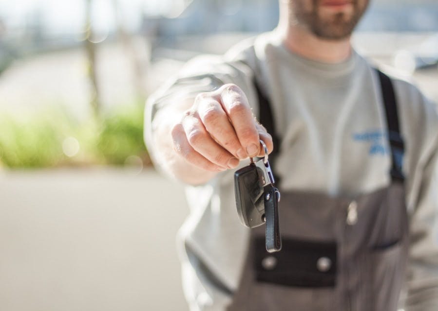 Automonteur steekt zijn hand uit en geeft een sleutel aan, zorg voor een goed onderhoud van je auto.