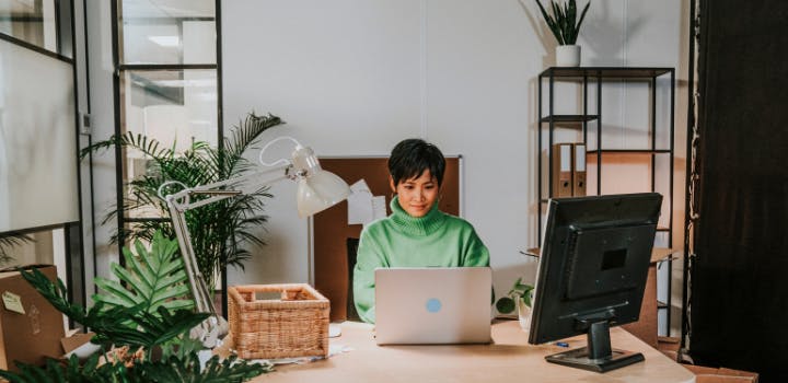 Vrouw zit achter een laptop met een groot extern scherm