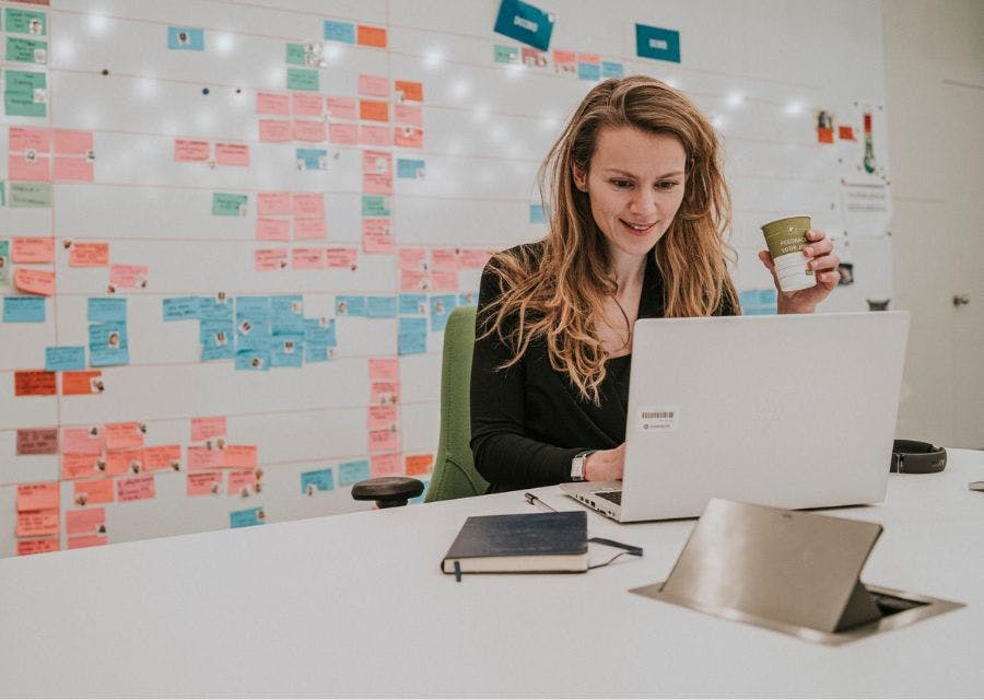 Vrouw achter laptop met achter zich een muur met post-its.