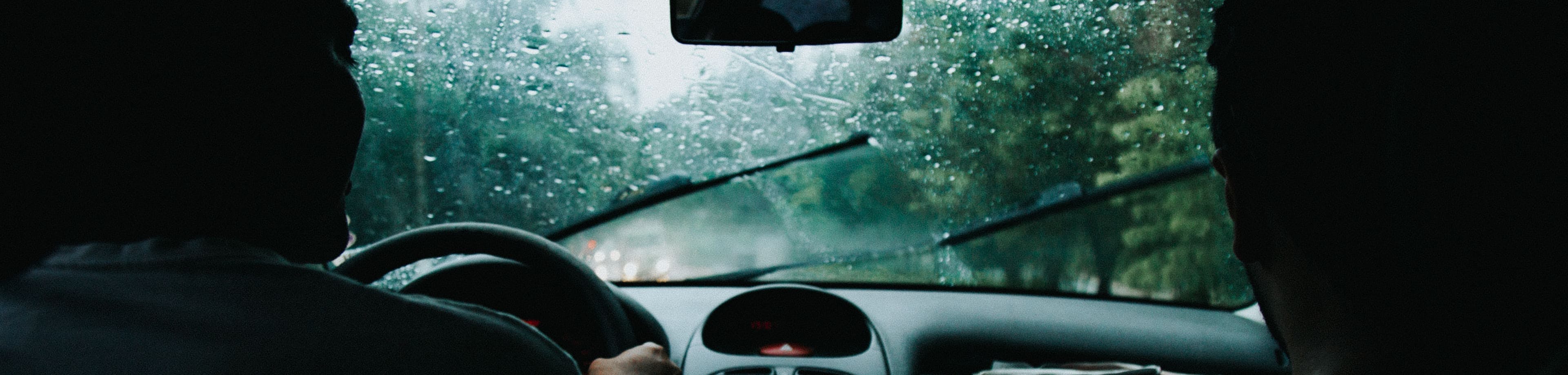 Voorruit van een auto met ruitenwissers tijdens een regenbui
