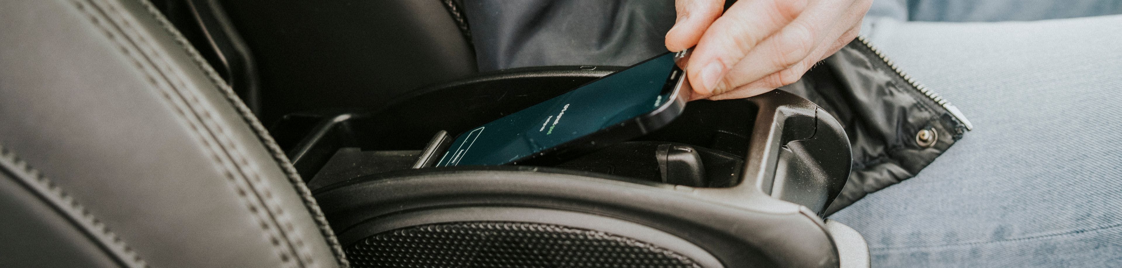 Iemand zit in de auto met de hand aan een telefoon die in de midden console ligt