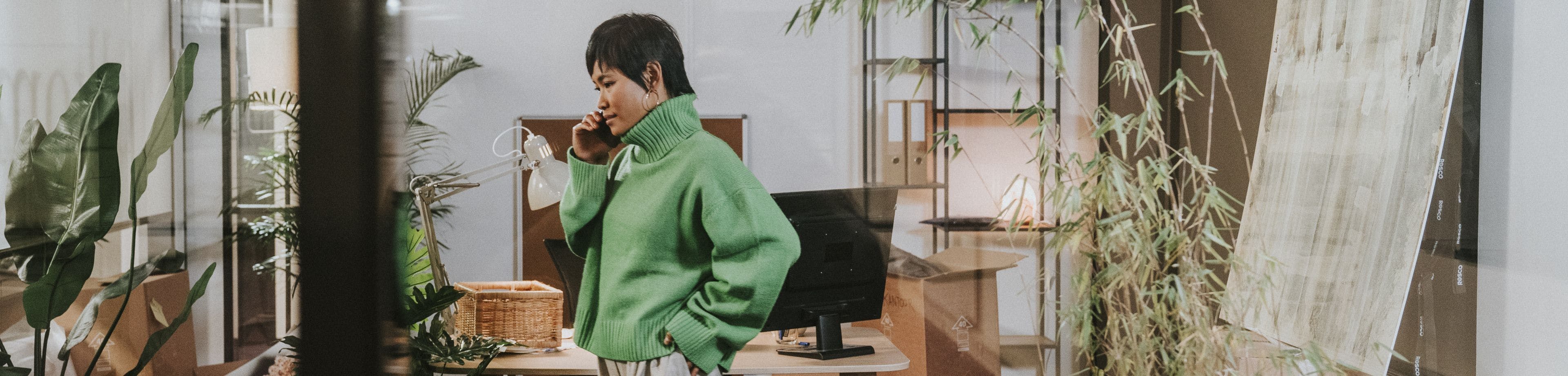 Iemand staat midden in een sfeervolle ruimte met veel planten en natuurlijke kleuren te bellen met een mobiele telefoon.