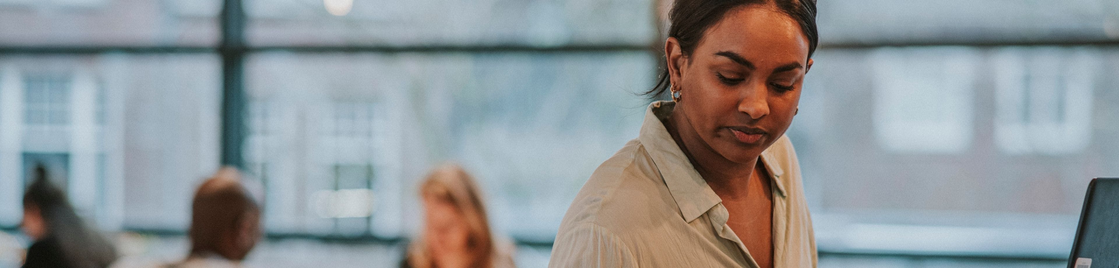 Een vrouw zit aan een werkplek en kijkt op haar mobiele telefoon.