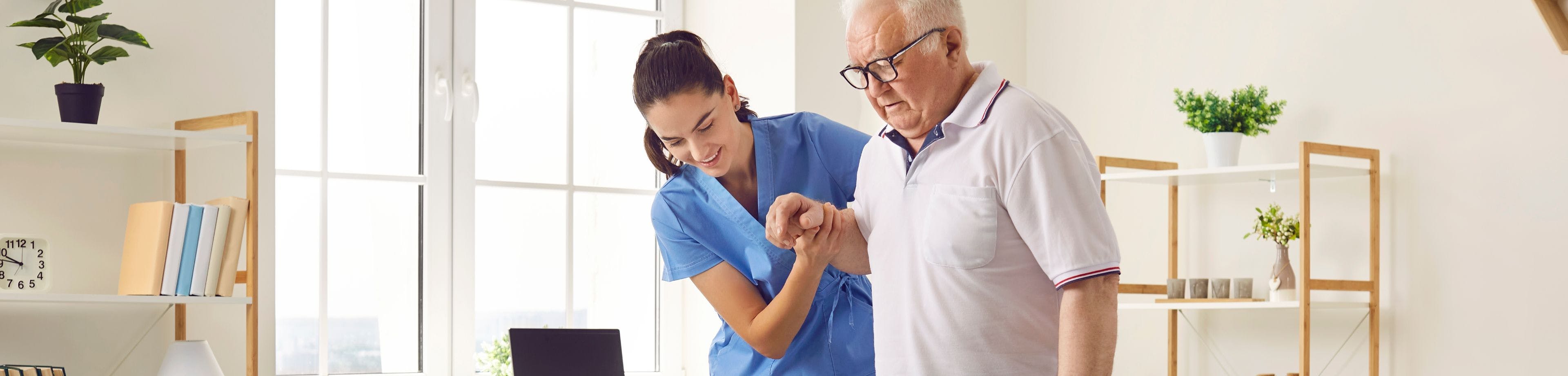 Een foto van een zorgverlener die een oudere man helpt met lopen.