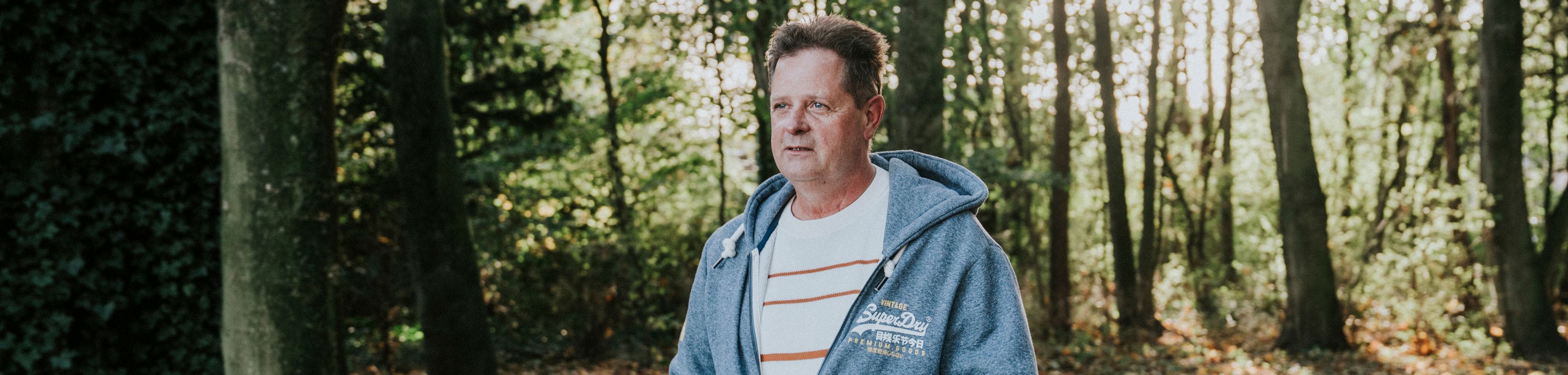 Kees Nieuwstraten op een zonnige dag in een bosrijke omgeving.