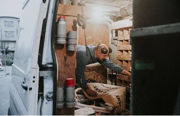 Een man in een werkoverall is bezig met het verzamelen van gereedschap uit zijn bedrijfswagen.
