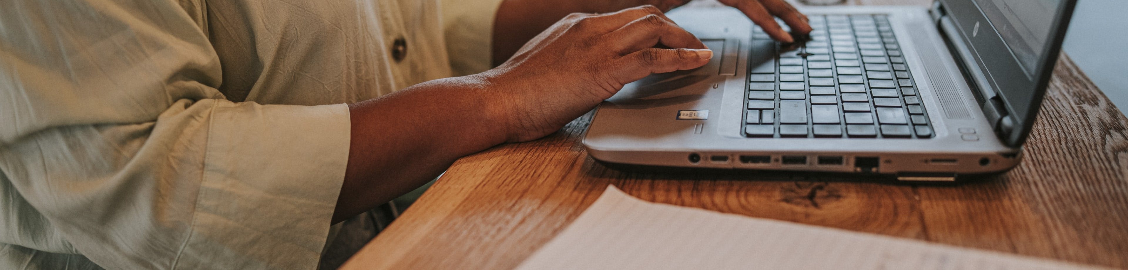 De handen van een persoon raken het toetsenbord van een openstaande laptop aan.