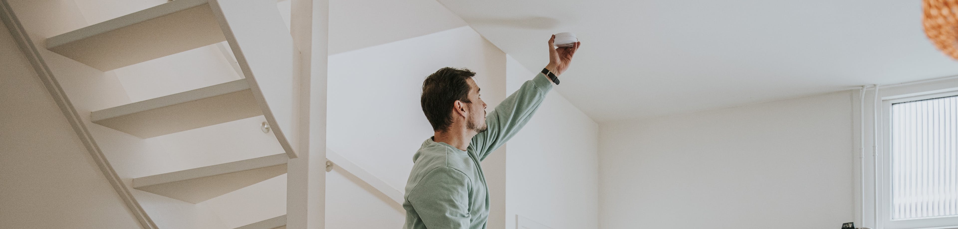 Een man draait aan een rookmelder, een vrouw staat erbij en wijst iets aan