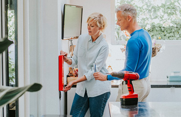 Een man en vrouw hangen een blusdeken op in huis.