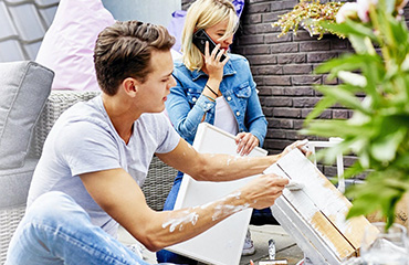 Man en vrouw zijn in de tuin een kastje aan het verven.