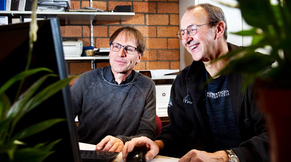 Erik Gommers en Corné Houtepen zitten samen lachend achter een computer