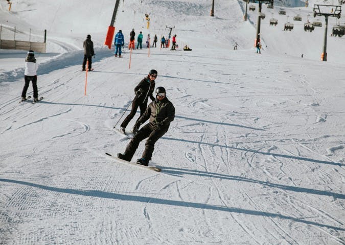 2 mensen dalen een berg af, de een op ski's, de ander op een snowboard.