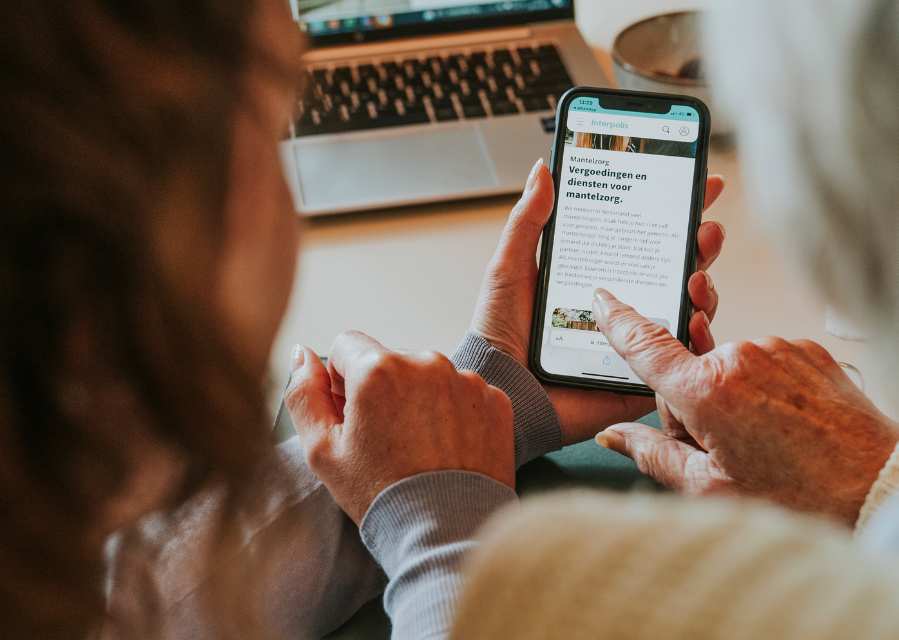 Een vrouw bekijkt met haar moeder de vergoedingen voor mantelzorg op haar telefoon.