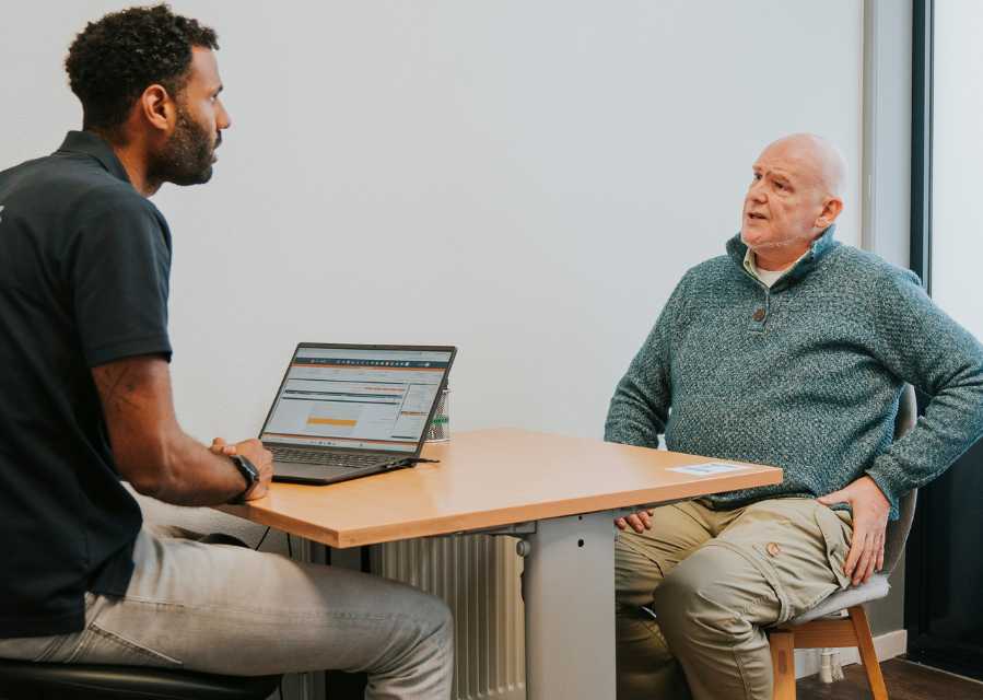 Een man zit aan tafel in gesprek met een fysiotherapeut.
