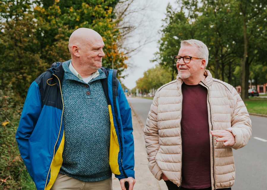 Twee mannen lopen op de stoep en zijn met elkaar in gesprek. 
