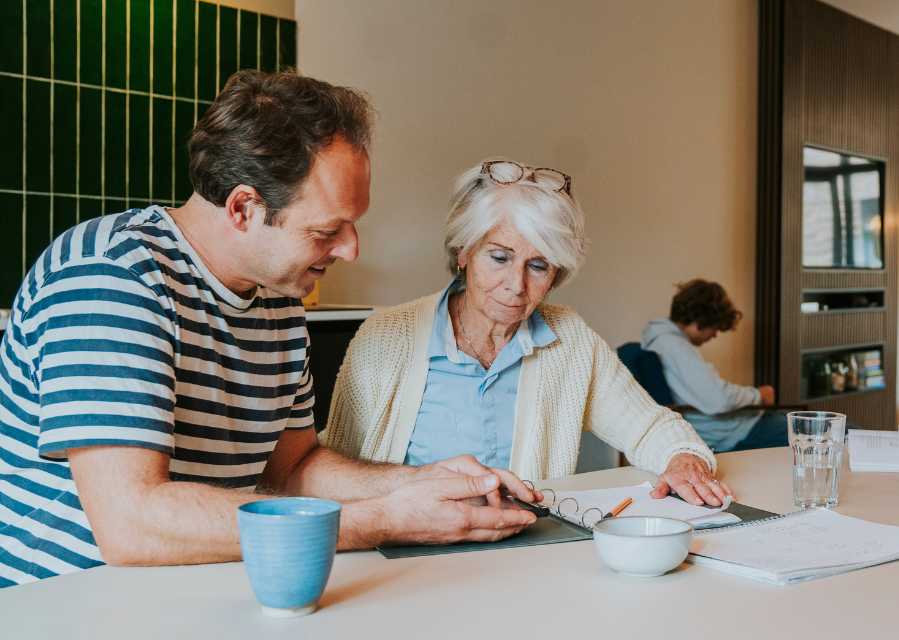 Vader en oma bekijken samen een map met documenten aan de eettafel. 