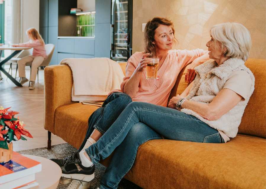 Moeder en oma zitten samen op de bank in de woonkamer. 