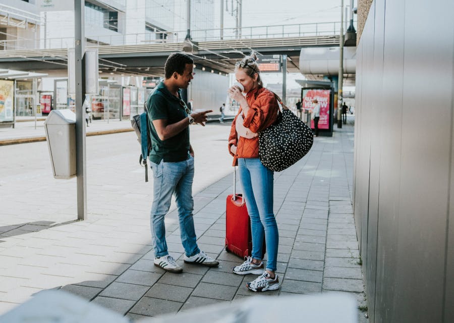 Een man en vrouw staan samen met hun bagage bij de bushalte.