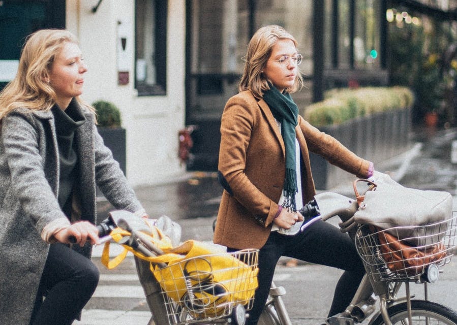 2 jonge meiden op de fiets, met een mandje voorop met hun tas erin