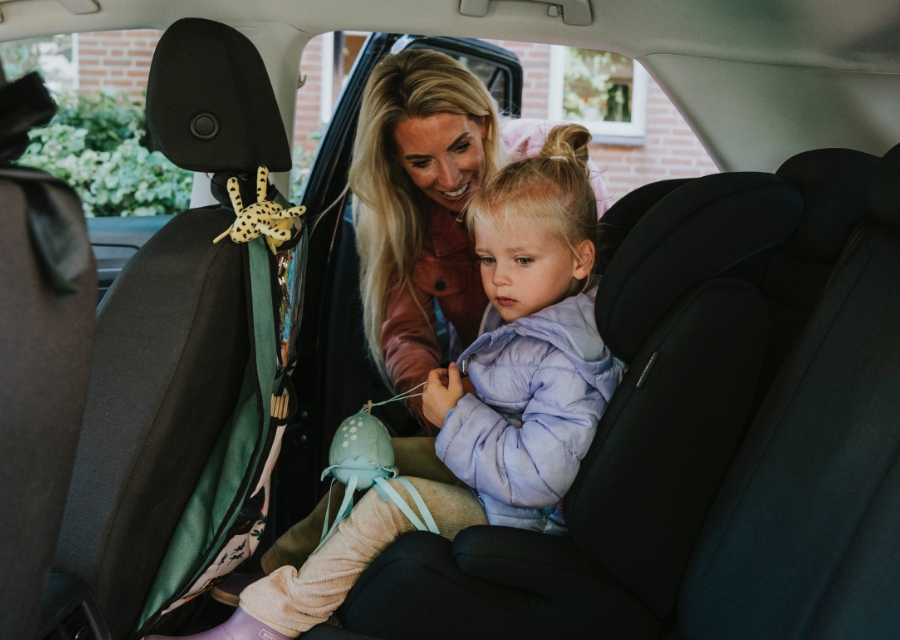 Moeder zet kind achterin de auto in een kinderzitje