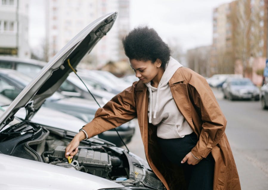 Vrouw staat bij een auto waarvan de motorkap open staat, zorg voor een goed onderhoud van je auto.