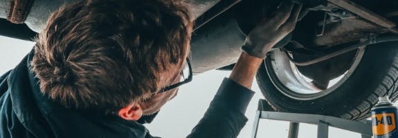 Man met bril sleutels aan de onderkant van een auto, zorg voor een goed onderhoud van je auto.