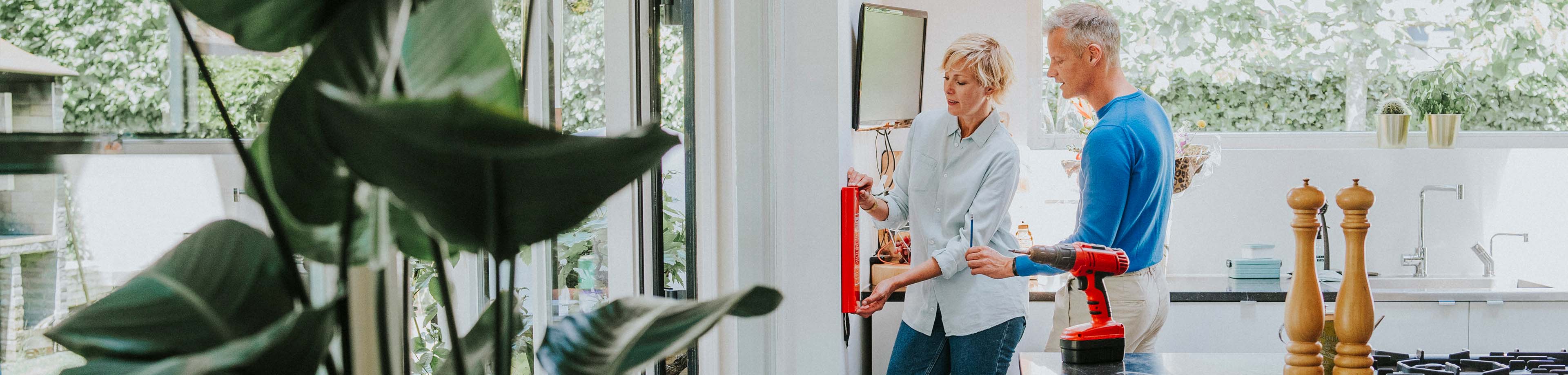 Een man en vrouw hangen een blusdeken op in huis.