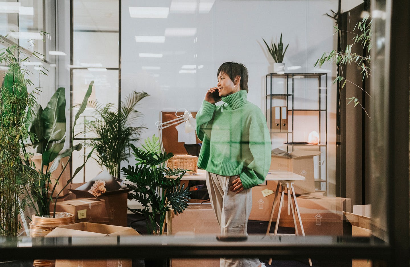 Een vrouw staat in een ruimte vol planten, te bellen met haar mobiele telefoon.
