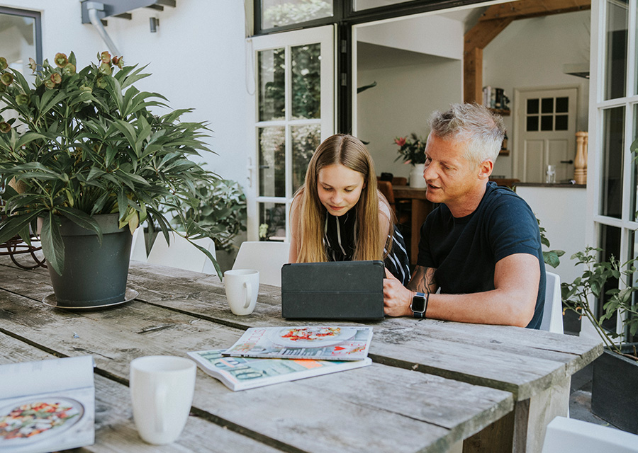 Vader en dochter zitten thuis aan de eettafel achter de tablet.