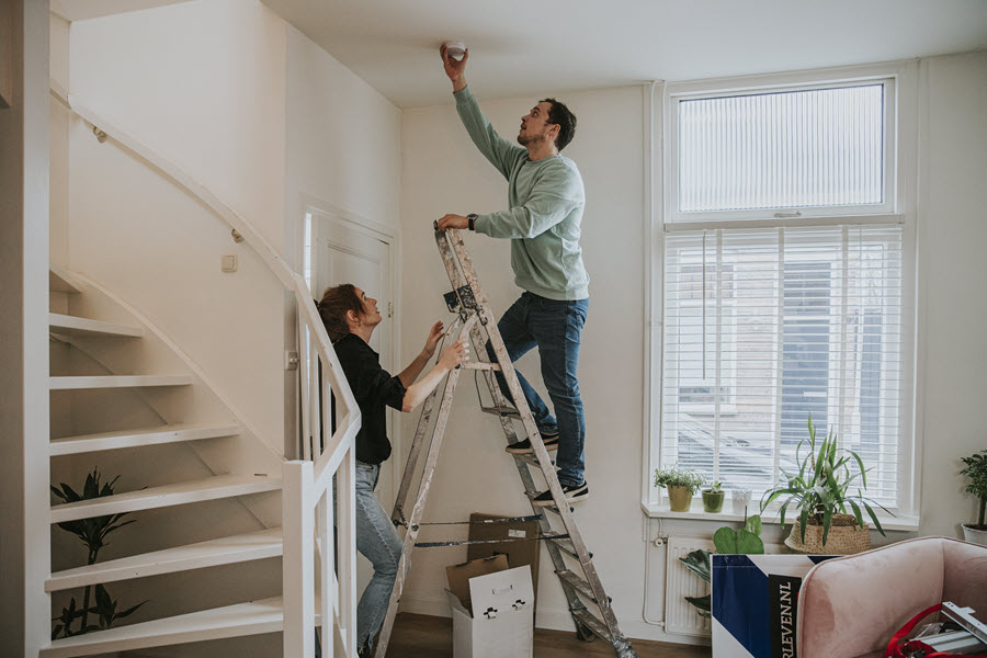 Een man en een vrouw maken hun woonkamer veiliger door samen een rookmelder op te hangen.