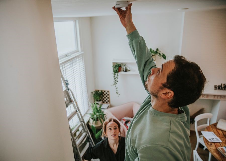 Een man hangt thuis zijn rookmelder op.