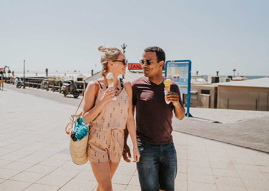 Een man en vrouw lopen over een boulevard en eten een ijsje