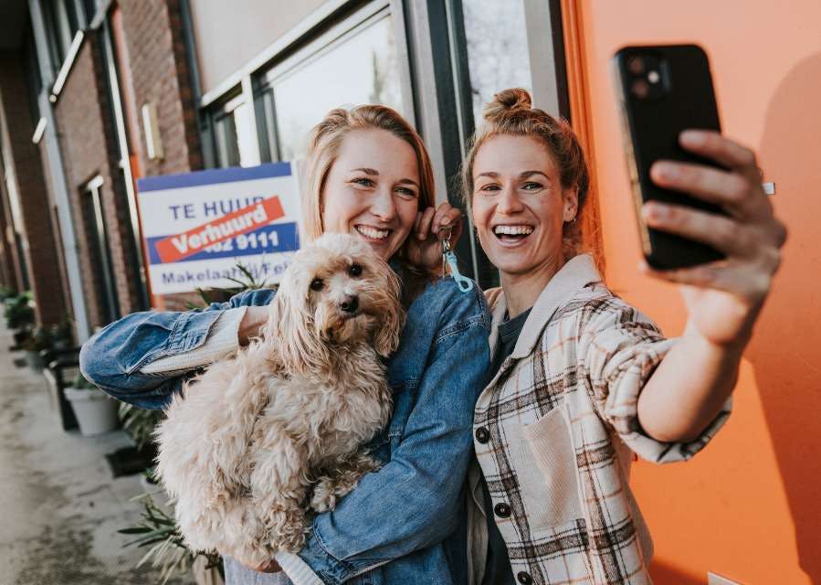 Twee vrouwen nemen samen lachend een selfie. Een van hen heeft een hond op de arm.