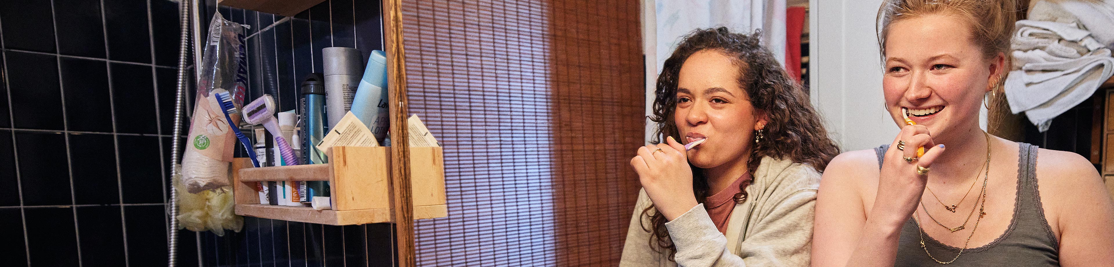 Twee studenten staan in de gezamenlijke badkamer naast elkaar en poetsen hun tanden met een tandenborstel.