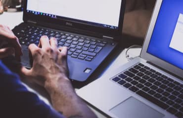 Een persoon die op twee laptops aan het werk is