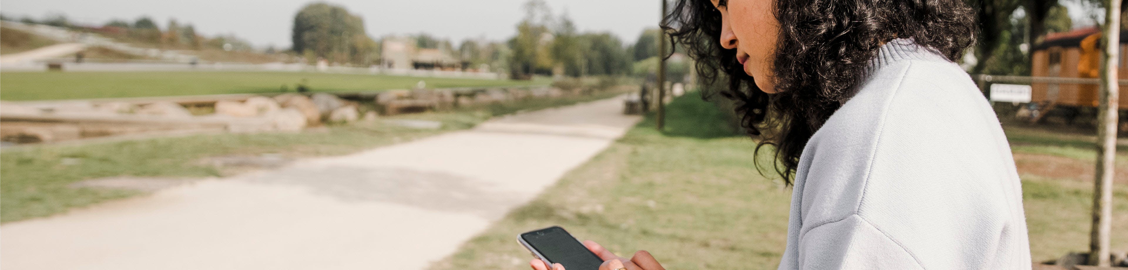 Een vrouw zit in een park en kijkt op haar smartphone.