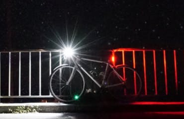 Fiets in het donker die, met fietsverlichting aan, tegen een railing staat