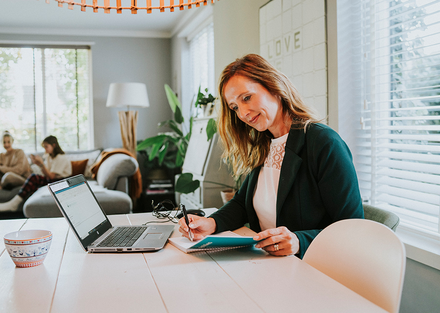 Vrouw zit aan de eettafel achter haar laptop.