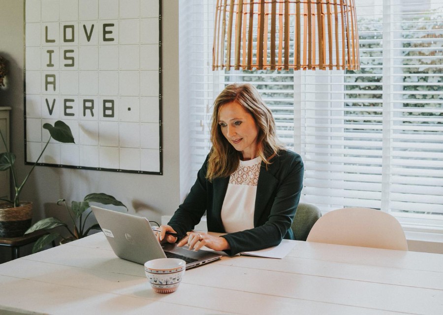 Een vrouw zit aan een tafel en werkt op haar laptop. 