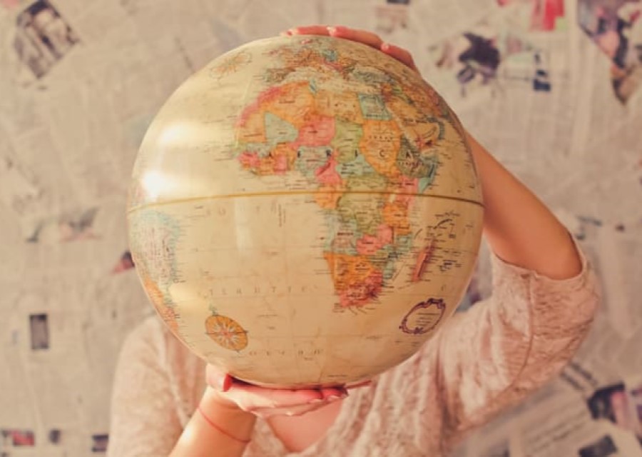 Een persoon houdt met 2 handen een wereldbol vast, en houdt die omhoog voor het gezicht. Van deze persoon zijn alleen de handen en armen te zien, het gezicht zit verstopt achter de wereldbol.