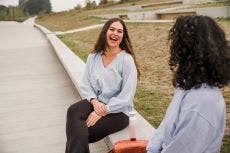 2 jonge vrouwen zitten samen op een bankje buiten en lachen