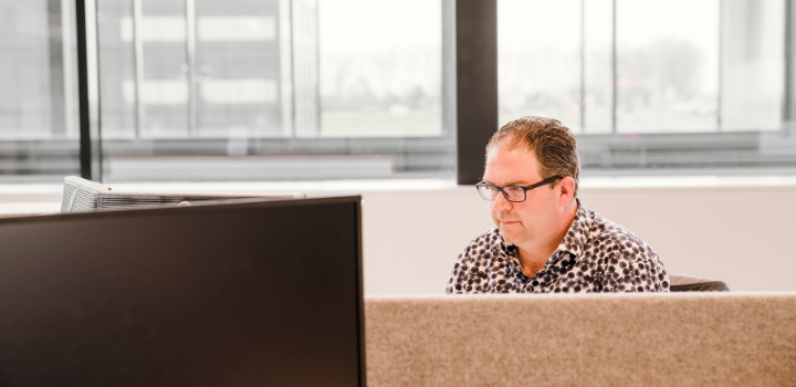 Een man achter een laptop in een kantoortuin