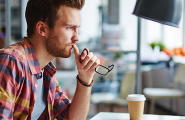 Man zittend aan een bureau, met een bril in zijn hand