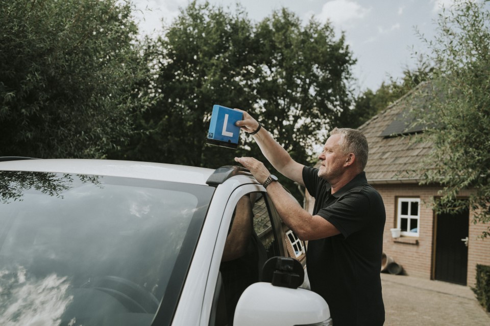 Rijschoolhouder bij zijn lesauto die wil weten of een AOV voor hem verplicht is.