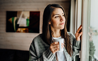 Vrouw staat voor het raam met een kop thee en kijkt naar buiten