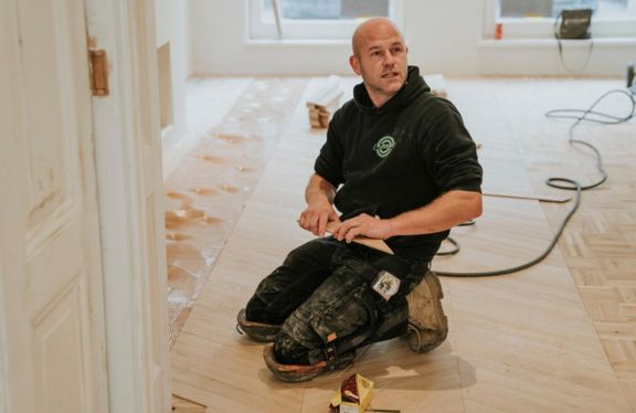 Vloerenlegger zit op zijn knieën.