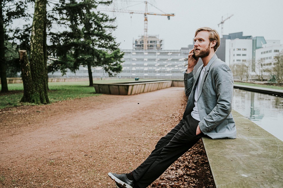 Een man zit bellend op de rand van de vijver in een park