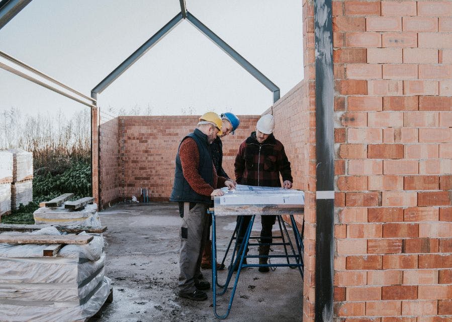 3 mannen met bouwhelmen kijken naar een bouwtekening op een bouwplaats