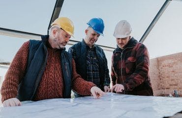 3 mannen met bouwhelmen kijken naar een bouwtekening op een bouwplaats